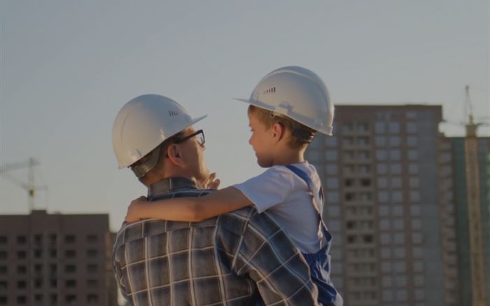 Mann und Kind mit Bauhelmen vor einer Baustelle